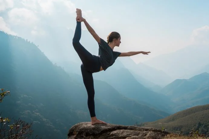 silhouette of lady doing yoga against mountainous background