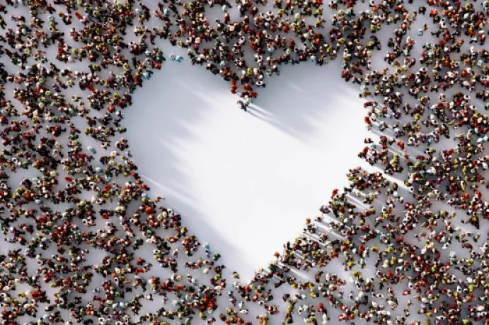 hundreds of people viewed from above to make the shape of a heart on a white floor