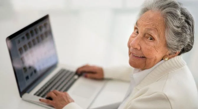 grey haired lady smiling working on laptop computer