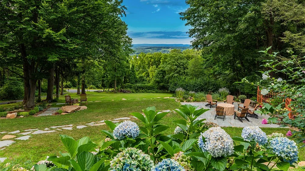 Exterior grounds with flowers, firepit, and stone paths surrounded by trees