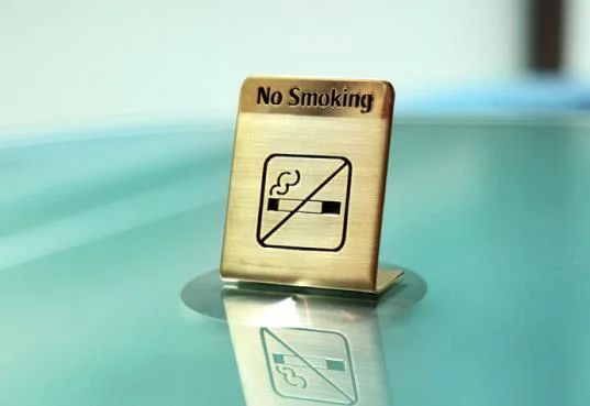 small brass no smoking sign on teal desk