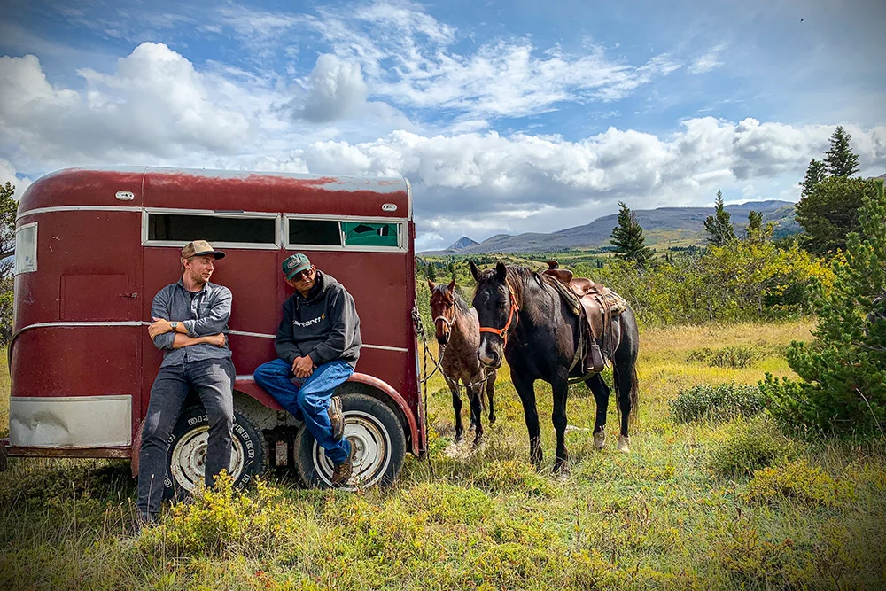 Experienced Travelers sitting on Horse Trailer with black and brown horse