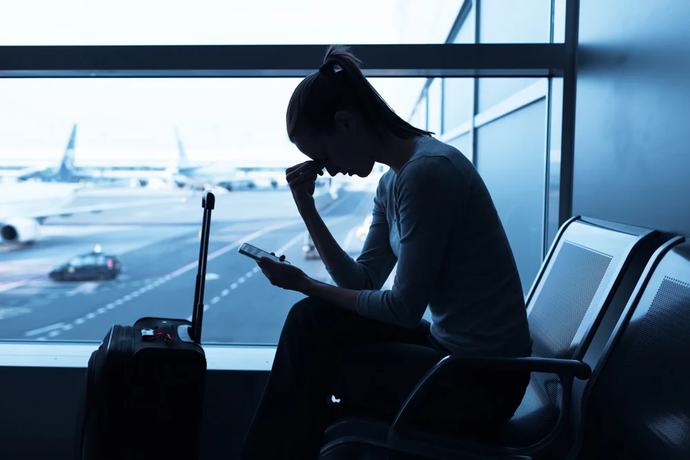 woman at airport looking at phone which shows missed flight