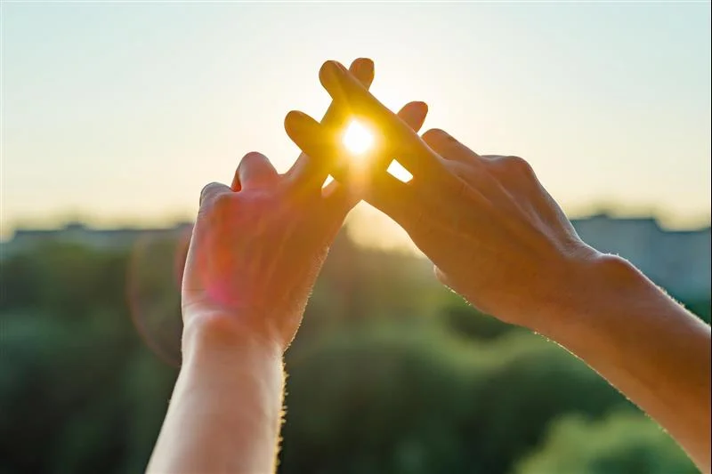 Woman forms a hashtag symbol with two fingers from each hand over the setting sun