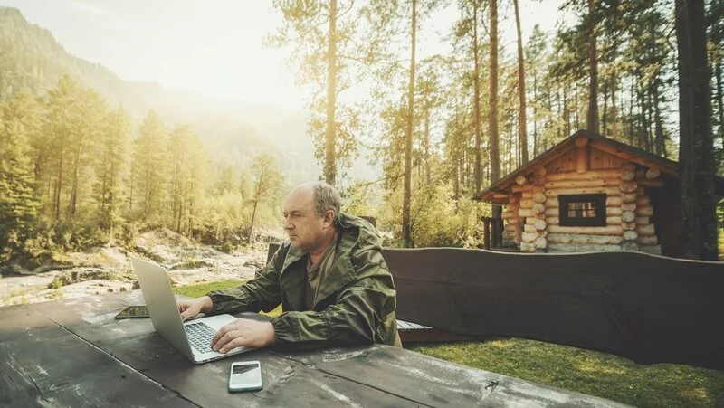 man working on laptop near cabin in woods